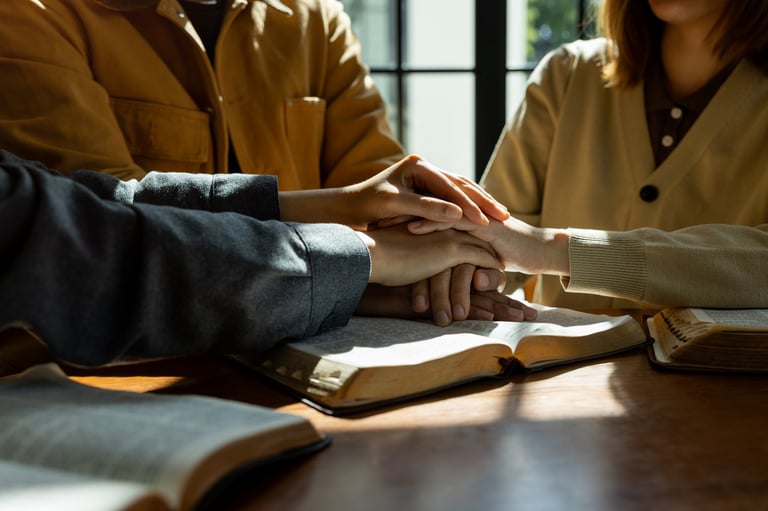 Christian group of people holding hands praying together over the Bible
