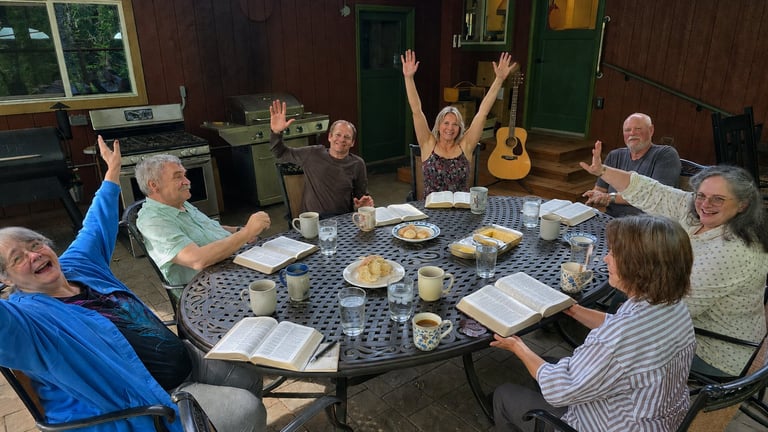 Group of people gathered around a round dining table indoors, eating and socializing together